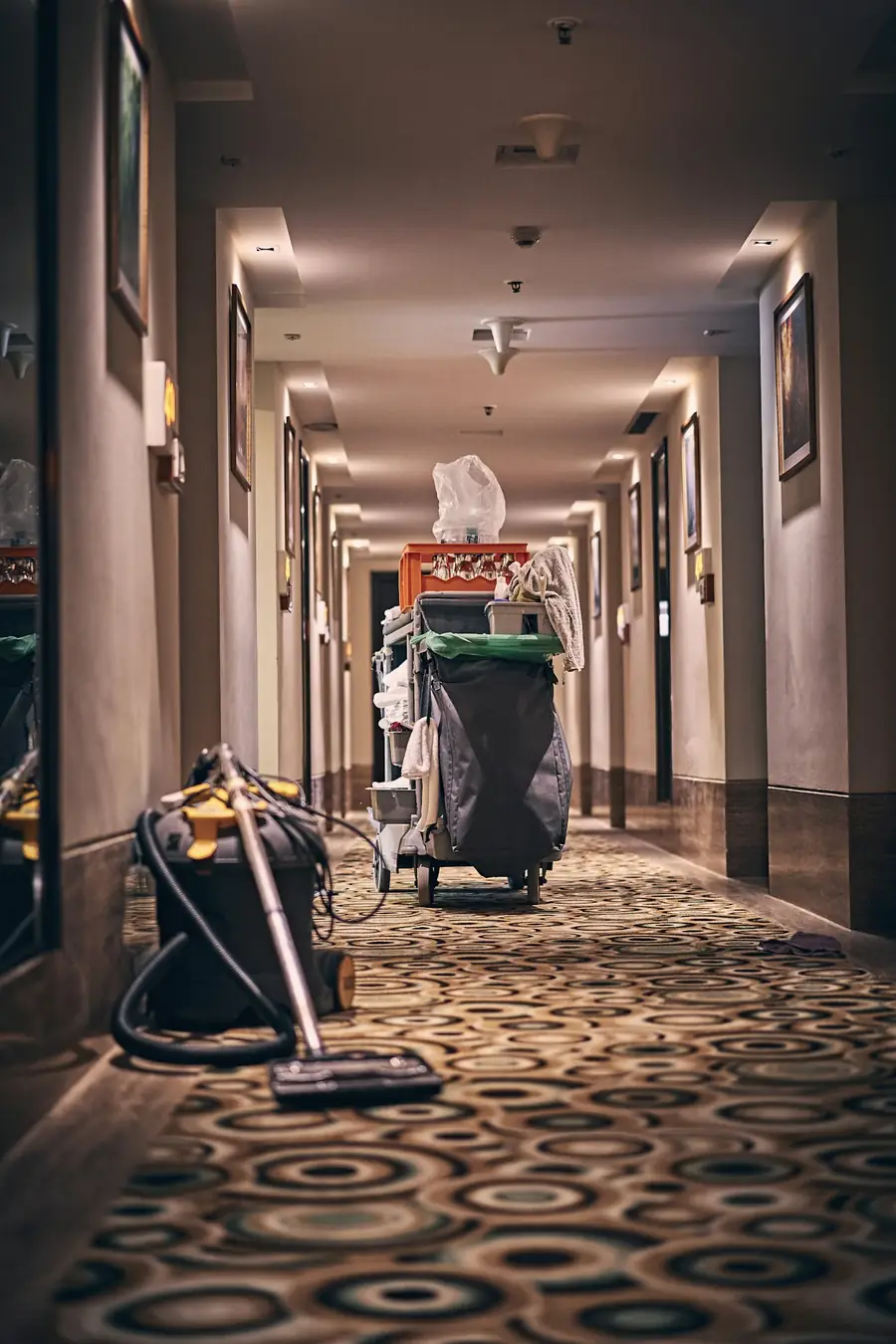 Hotel housekeeping cart and vacuum cleaner in a long carpeted hotel corridor