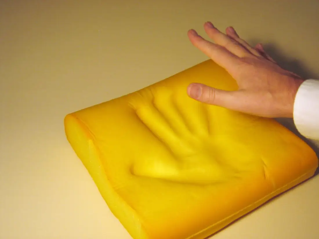 Hand pressing into a yellow memory foam pillow, leaving a handprint in the foam