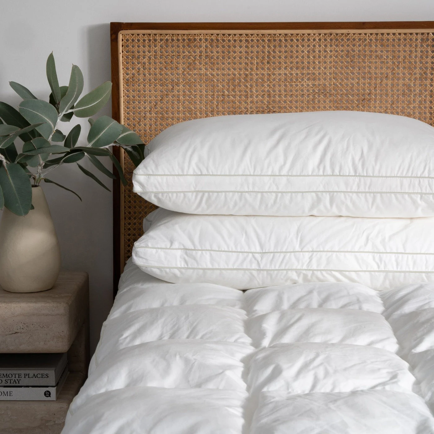 Two white Suite Supply Co. Signature Deluxe Suite Pillows stacked on a bed with a cane headboard